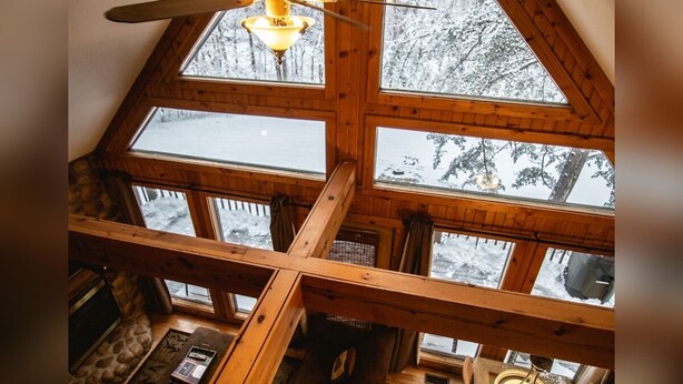 Ein Zimmer mit hohen Decken, Holzbalken, großen Fenstern und einem Deckenventilator.