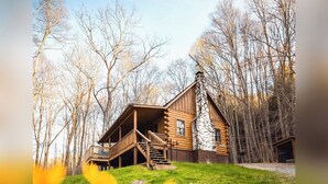 Une cabane en rondins dotée d’une véranda et d’un escalier, entourée d’arbres.