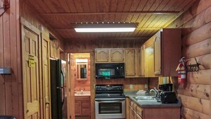 L’intérieur d’une cabane en bois comprend une table à manger, des chaises, une cuisine avec des meubles en bois, un réfrigérateur, un four, un four à micro-ondes et un évier.