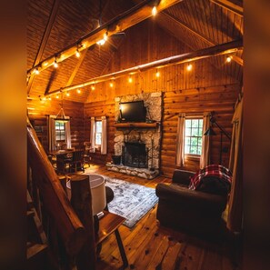 Un acogedor interior de cabaña de madera con chimenea de piedra, paredes de madera y zona de comedor.