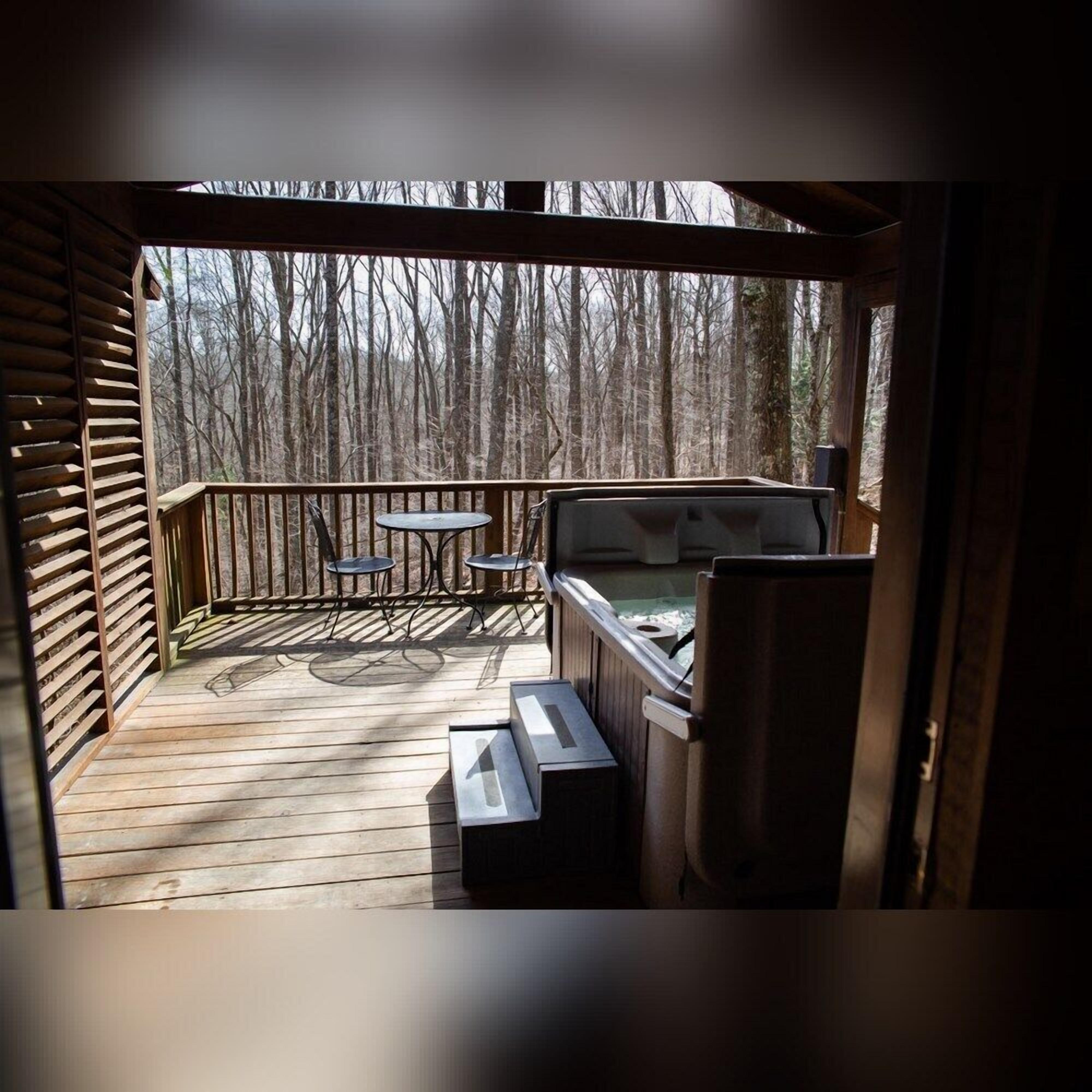 A wooden deck with a hot tub, two small tables, and a bench.