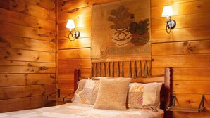 Ein Zimmer in einer Holzhütte mit einem Bett, zwei Wandlampen und einem Wandteppich.