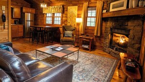 Ein gemütliches Cabin-Interieur mit Kamin aus Stein, Holzbalkendecke und einem Essbereich mit Tisch und Stühlen.
