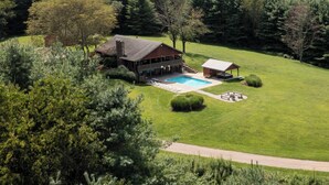 Una casa grande con piscina, rodeada de césped cuidado y árboles.