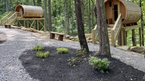 Twee houten boomhutten met houten trappen en een bankje, gelegen in een bos.