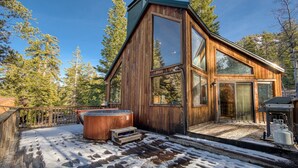 Una cabaña de madera con ventanas amplias, un jacuzzi y una terraza.