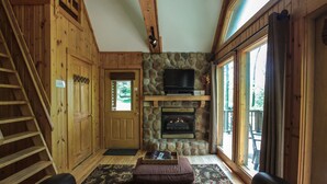 A cozy cabin interior with a stone fireplace, wooden walls, a staircase, and a comfortable seating area. - Laurelwood - Hosted by The Chalets (Logan)