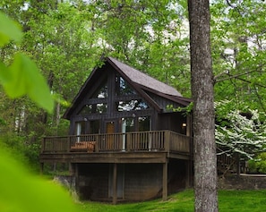 Situated in a lush forest, this cabin features a traditional design with a steeply pitched roof and a large front door.