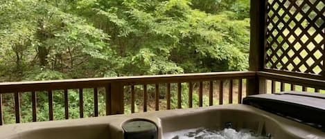 Een hottub met een houten terras en uitzicht op een bos.