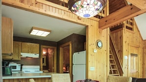 A dining area with a glass-top table, wicker chairs, a wooden ceiling, and a stained glass light fixture. - Laurelwood - Hosted by The Chalets (Logan)