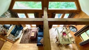 A cabin with a loft bedroom, a stone fireplace, a dining area, and a view of the forest. - Laurelwood - Hosted by The Chalets (Logan)