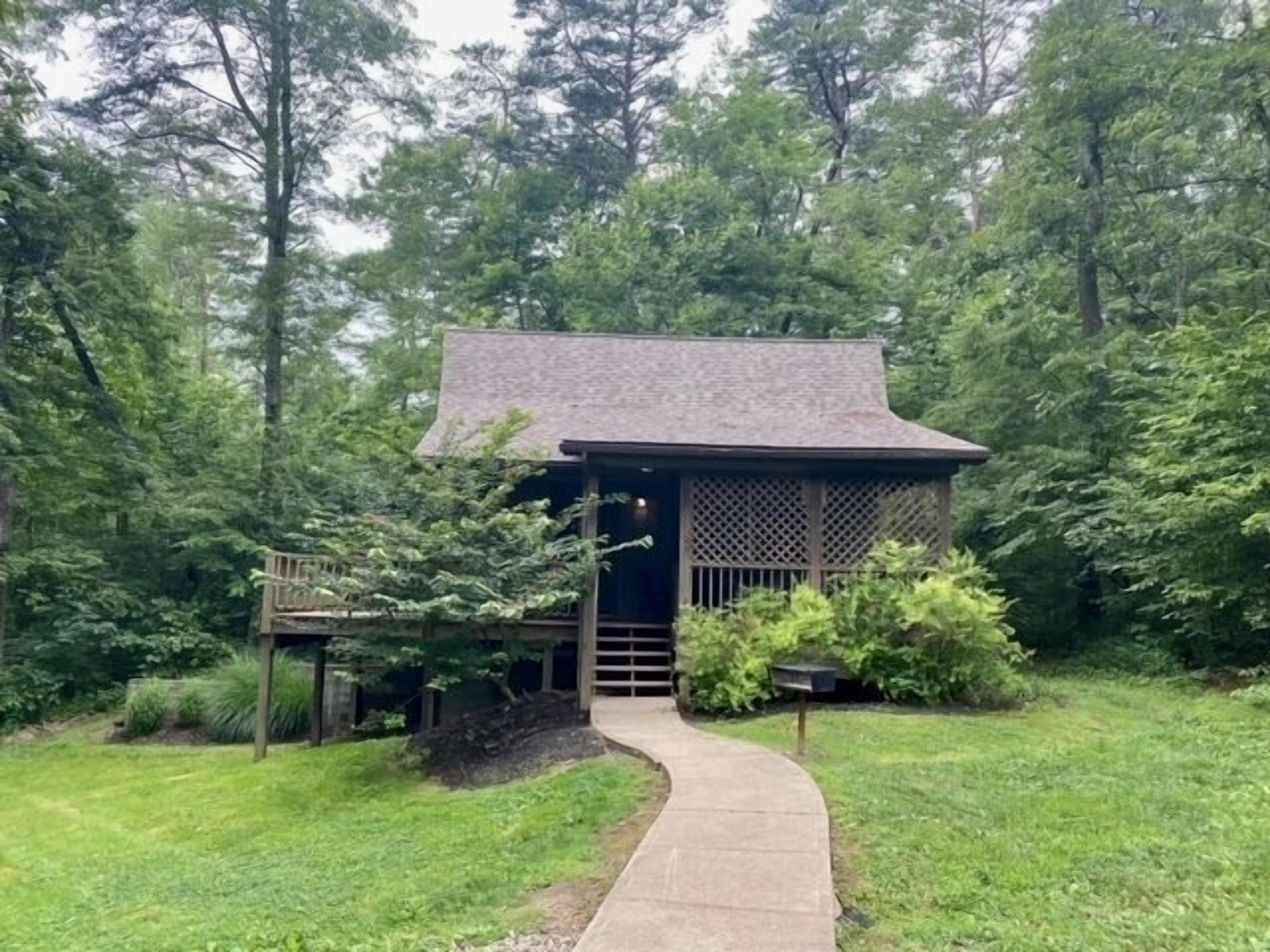 Eine kleine Holzhütte mit geneigtem Dach, umgeben von dichtem Wald.