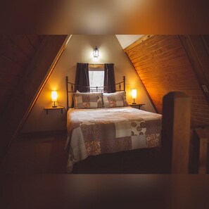 A cozy attic bedroom with a bed, two bedside lamps, and a window with curtains. - A-Frame #04 - Hosted by The Chalets (Logan)