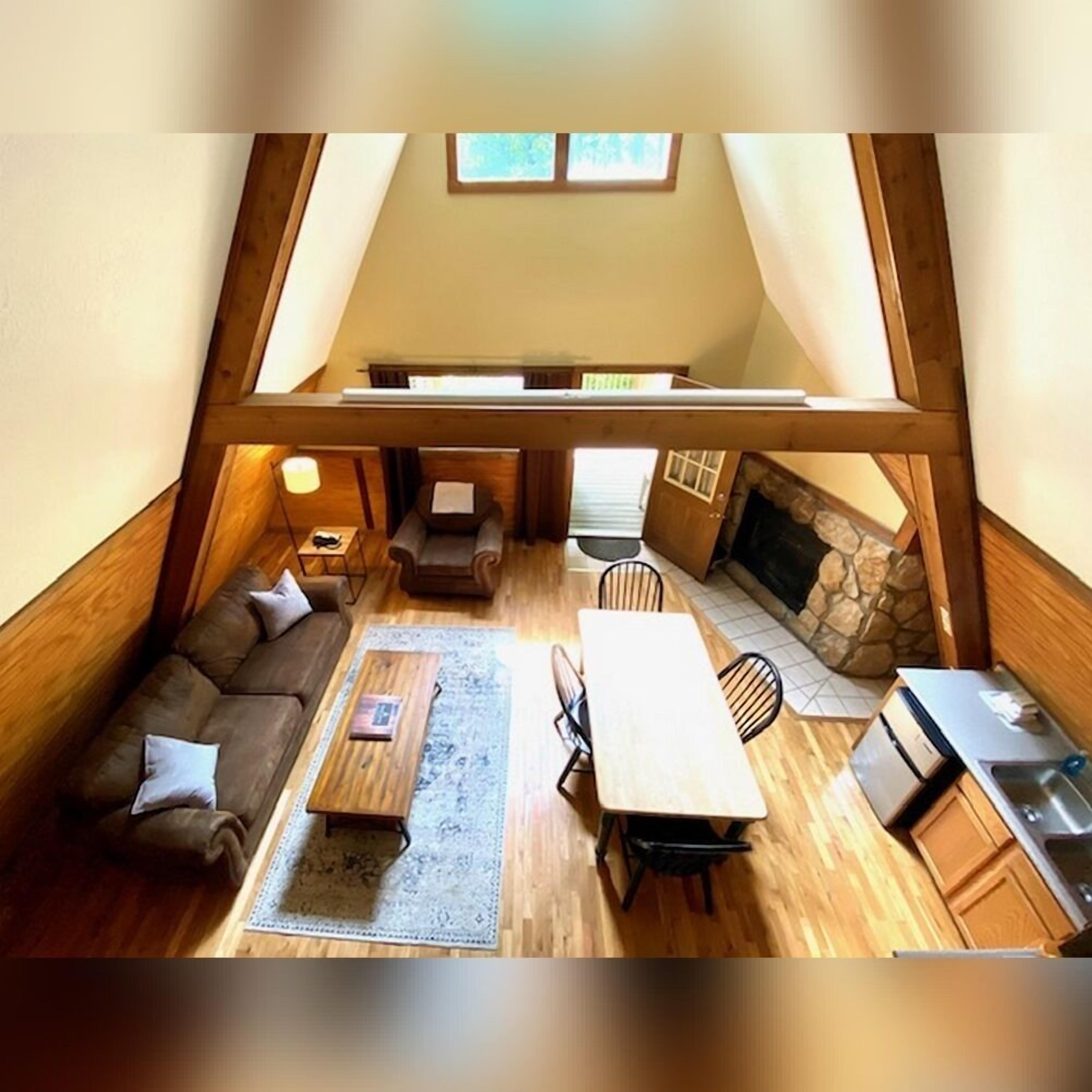 A loft-style room with a wooden ceiling, a sofa, a coffee table, a fireplace, and a dining area.