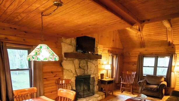 A cozy cabin interior with a wooden dining table, chairs, a fireplace, and a living area with a sofa and armchairs. - Sycamore - Hosted by The Chalets (South Bloomingville)