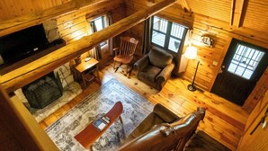 A cozy cabin interior with a fireplace, wooden floors, a dining area, and a staircase. - Sycamore - Hosted by The Chalets (South Bloomingville)