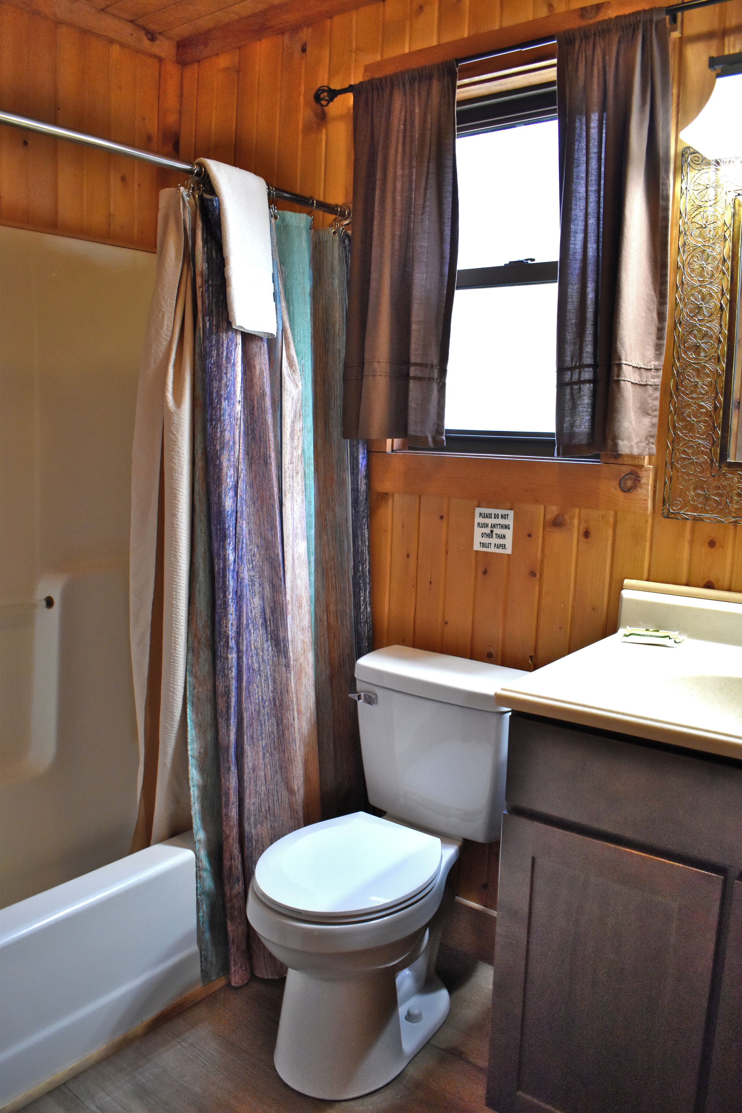 A bathroom with a bathtub, toilet, and a window with curtains.