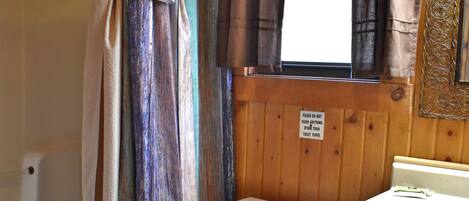A bathroom with a bathtub, toilet, and a window with curtains.
