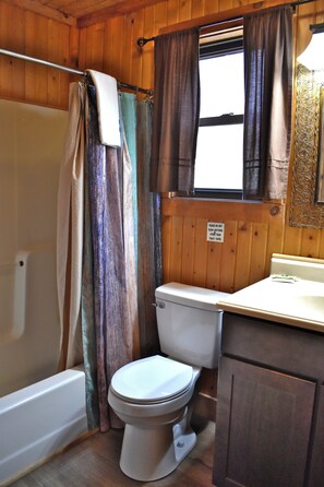 Ein Badezimmer mit Badewanne, Toilette und einem Fenster mit Vorhängen.