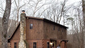 A rustic log cabin with a stone chimney, a wooden porch, and a gravel path leading to it. - Sycamore - Hosted by The Chalets (South Bloomingville)