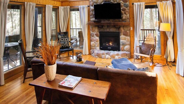A spacious living room with a stone fireplace, large windows, and a cozy seating area. - The Ravine - Hosted by The Chalets (Logan)