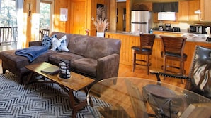 A spacious living area with a high ceiling, a wooden balcony, a kitchen with modern appliances, and a cozy seating area. - The Ravine - Hosted by The Chalets (Logan)