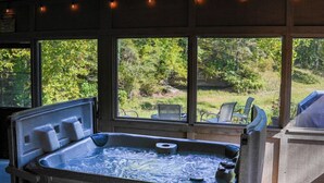 Een hottub met een stenen buitenkant, omringd door grote ramen met uitzicht op een weelderige tuin.