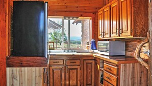 Cocina de cabaña de madera con un ventanal grande, armarios de madera, un microondas y un lavaplatos.