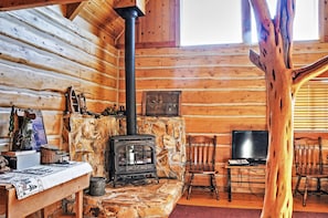 A log cabin interior with a stone fireplace, wooden walls, a television on a table, and a bench. - Remote Antimony Log Cabin w/ Green Meadow Views! (Antimony)
