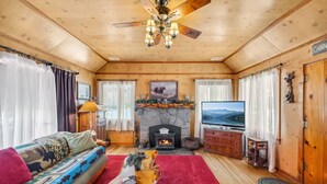 Ein gemütliches Blockhauss-Interieur mit Holzbalkendecke, Kamin, Fernseher und einer Couch mit Decke.