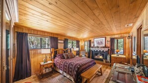 Ein gemütliches Schlafzimmer in einer Holzhütte mit einem großen Bett, einer hölzernen Bank, einem Kamin und einem Fenster mit Blick auf den Wald.
