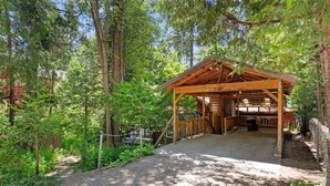 Eine Holzhütte mit einer Laube, umgeben von dichtem Wald.