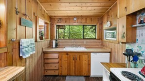 Eine kompakte Küche mit Holzausstattung, einem Spülbecken, einem Geschirrspüler und einem Fenster mit Blick auf Grünfläche.