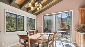 A dining area with a wooden table and chairs, large windows, and a view of the outdoors. - On the Edge at Alpine By Tahoe Getaways - Dog OK- Mountain Views- Ski Shuttle! (Alpine Meadows)