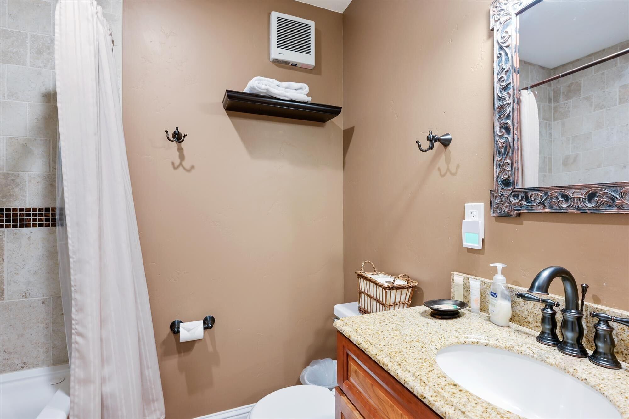 A bathroom with a beige wall, a white toilet, a sink with a granite countertop, a mirror with an ornate frame, and a towel rack with a towel.