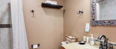 A bathroom with a beige wall, a white toilet, a sink with a granite countertop, a mirror with an ornate frame, and a towel rack with a towel.