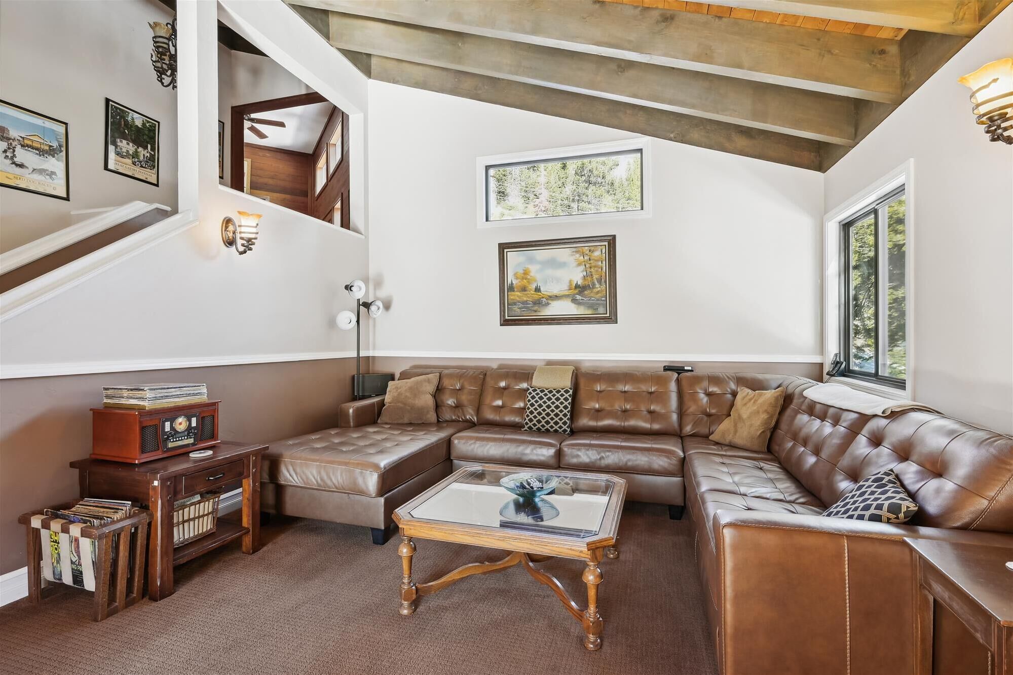 Ein geräumiges Wohnzimmer mit einem großen braunen Ledersofa, einem Glastisch und einer Holz-Unterhaltungsanlage mit Schallplatten.