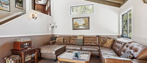 Ein geräumiges Wohnzimmer mit einem großen braunen Ledersofa, einem Glastisch und einer Holz-Unterhaltungsanlage mit Schallplatten.