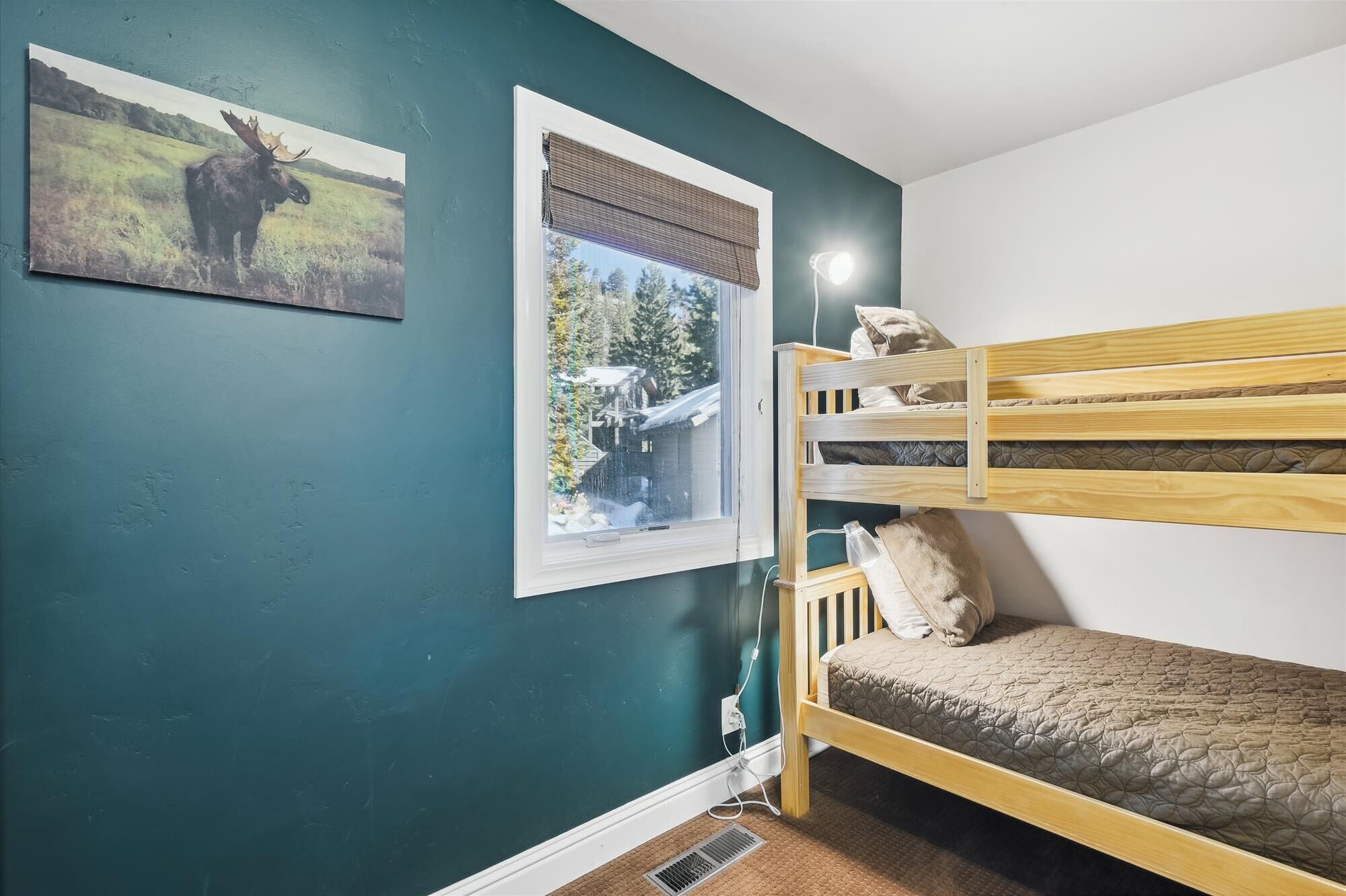 A room with teal walls, a bunk bed, two framed pictures, and a window with a view of trees and a building.