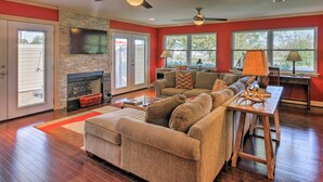 A spacious living room with a fireplace, a large sofa, a coffee table, and a TV mounted on the wall. - Pottsboro Home on 2 Acres w/ Hot Tub, Near Marina! (Pottsboro)