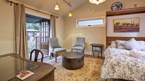 Habitación de hotel con cama, dos sillones, un otoman redondo, una mesa y ventana con vista a zonas verdes.