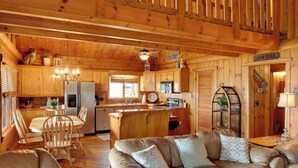 Interior de una cabaña con una zona de comedor de madera, un sofá y una cocina equipada con refrigerador y pileta.