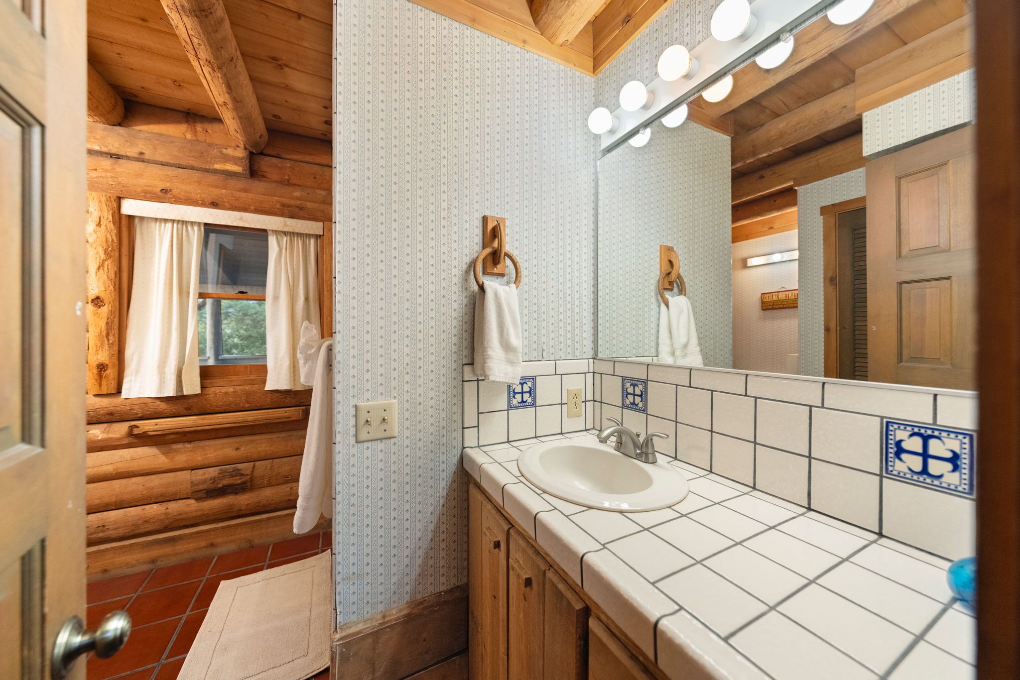 A bathroom with wooden walls, a white sink, and a mirror with lights.