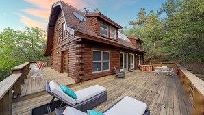 Una cabaña de troncos con una terraza, asientos exteriores y un ventanal grande.