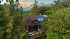 Una cabaña con terraza, paneles solares y el paisaje de una montaña al fondo.
