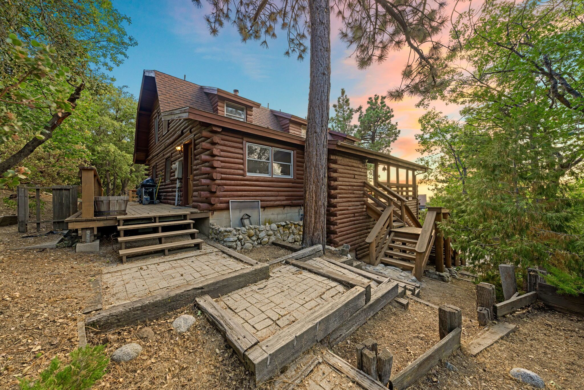 A rustic log cabin with a wooden deck and a staircase leading to the entrance.