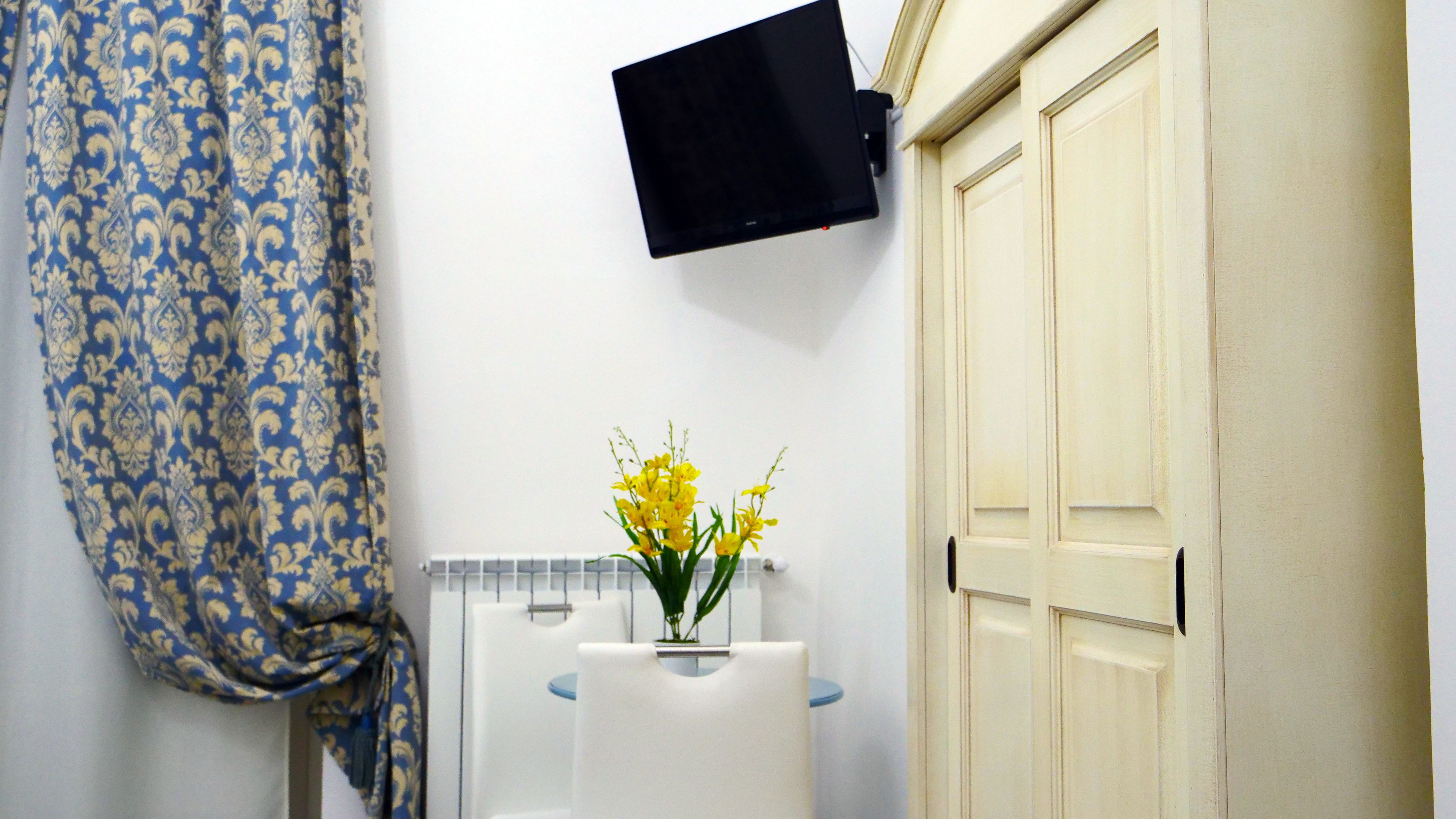Ein Badezimmer mit Duschvorhang, einem angebrachten Fernseher, einem Waschbecken mit Blumenvase und einer Tür.