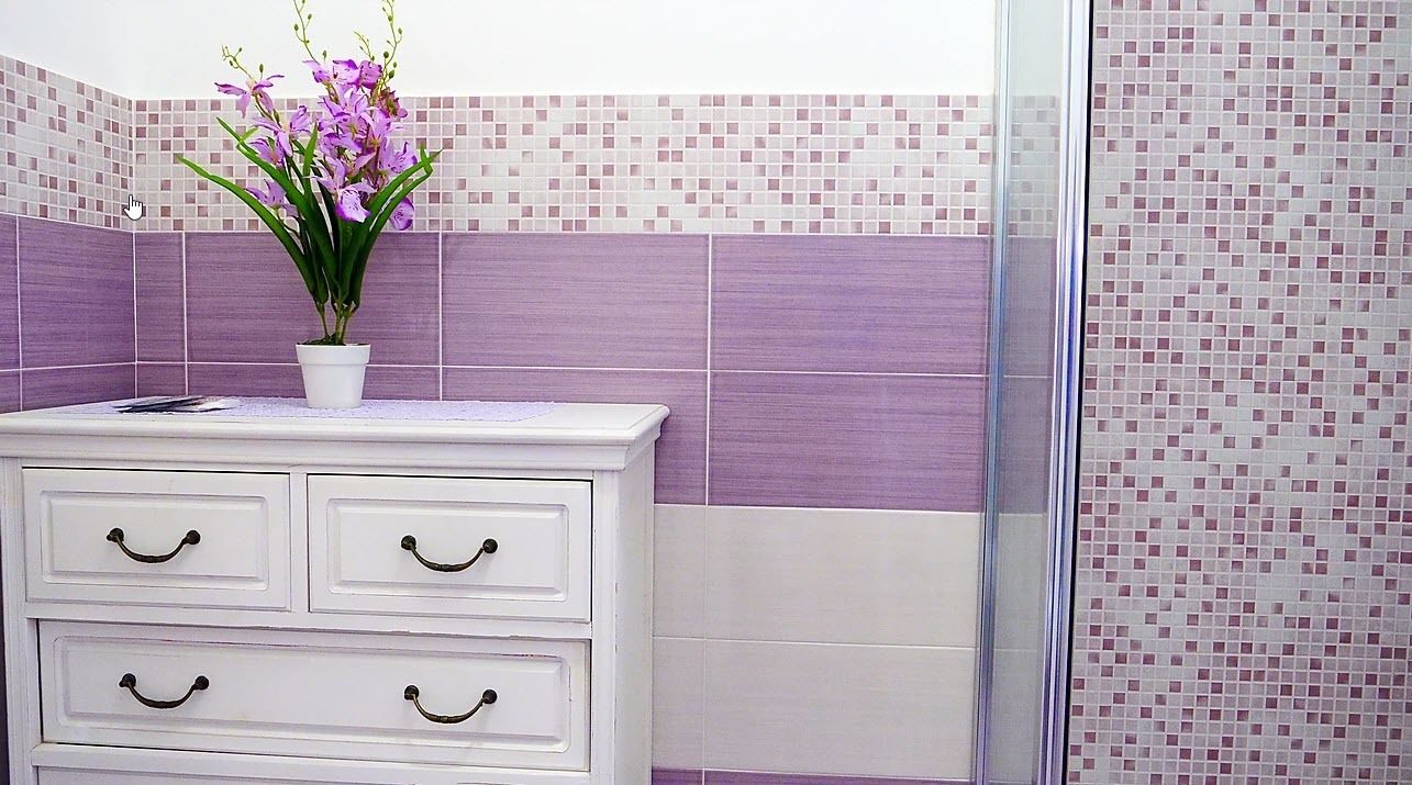 A bathroom with a white vanity, purple tiled walls, and a glass shower enclosure.