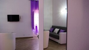 Una sala de estar moderna con un televisor de pantalla plana montado en la pared, un sofá gris con cojines, un sillón blanco y suelo de madera.