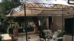 Un espacio de estar al aire libre con techo, mobiliario blanco y una pérgola.